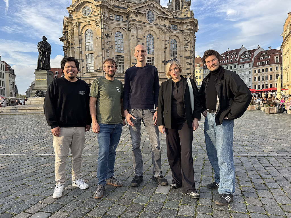 Fünf Personen stehen auf einem Platz vor der Frauenkirche ein Dresden