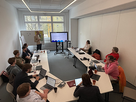 Gruppe von Workshop-Teilnehmenden schaut Mann bei Präsentation zu.